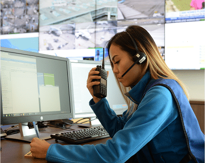 a woman sitting infront of a computer holding a two way radio and wearing a headset.