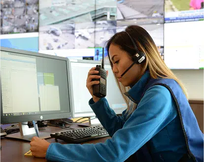 a woman sitting infront of a computer holding a two way radio and wearing a headset.