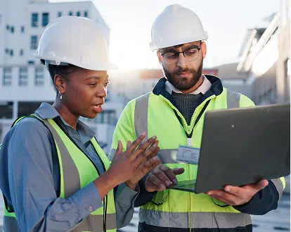 two people outside looking at a laptop wearing safety clothing.