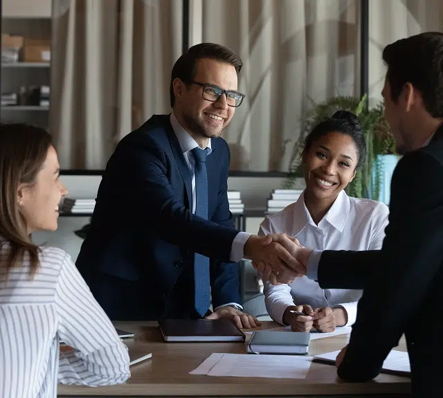 4 people in a board room 2 shaking hands over the table