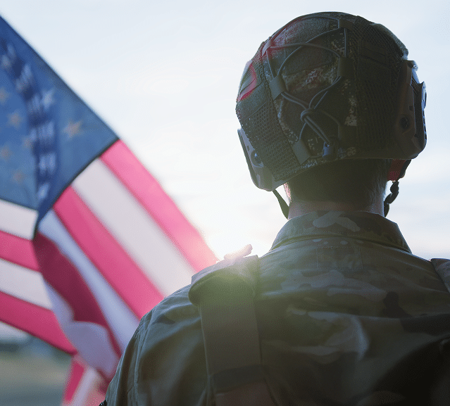 A soilder looking toward a sunset with an American flag in the foreground.
