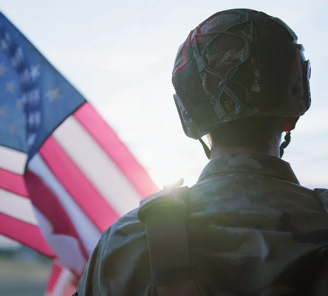 A soilder looking toward a sunset with an American flag in the foreground.