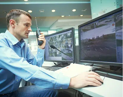 A man talking on a 2 way radio looking at computer screens