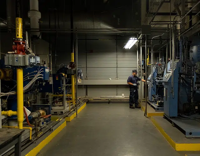 Technician inspecting industrial machinery in a dimly lit mechanical room.